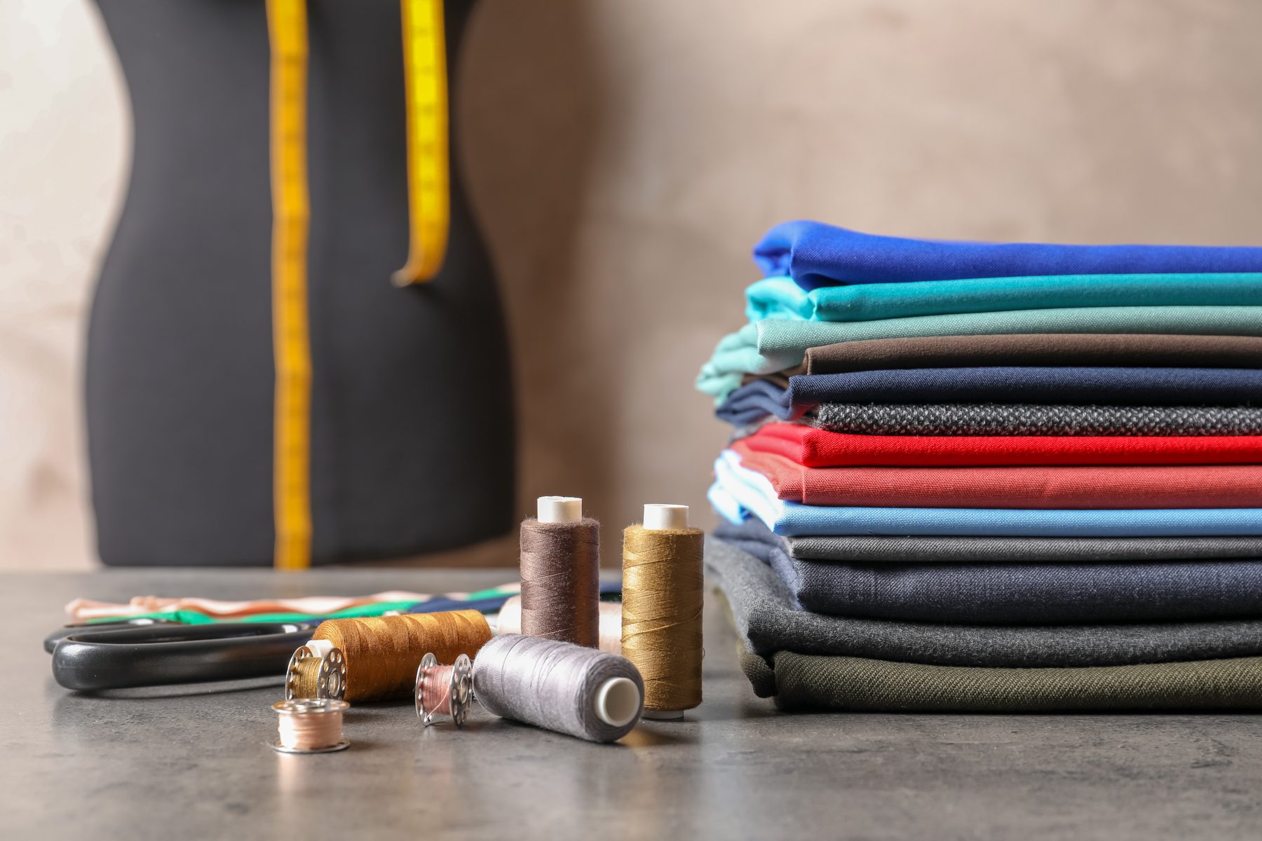 Bobines de fil, mètre ruban et pile de tissus sur la table d'un atelier de tailleur