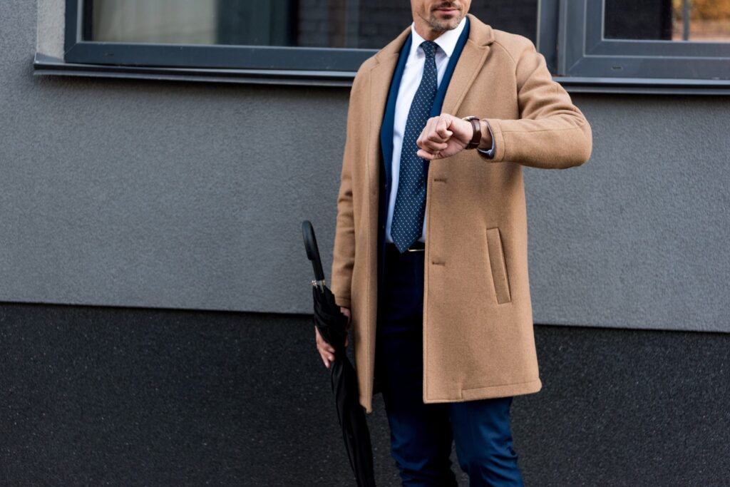 Homme en manteau camel long porté sur un costume bleu marine et une cravate
