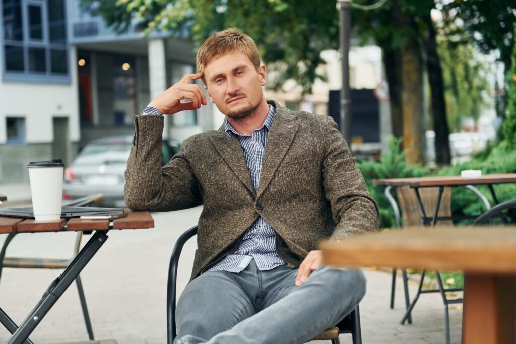Homme en veste de tweed chevron attablé à un café, chemise à carreaux