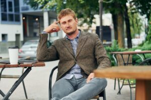 Homme en veste de tweed chevron attablé à un café, chemise à carreaux